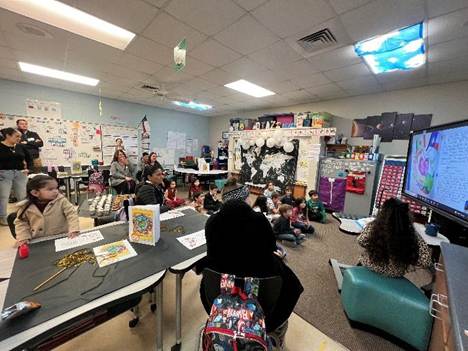 A vibrant classroom filled with students, teachers, and parents engaging in a multilingual writing celebration. A large screen displays student work as attendees participate in a lively learning environment.