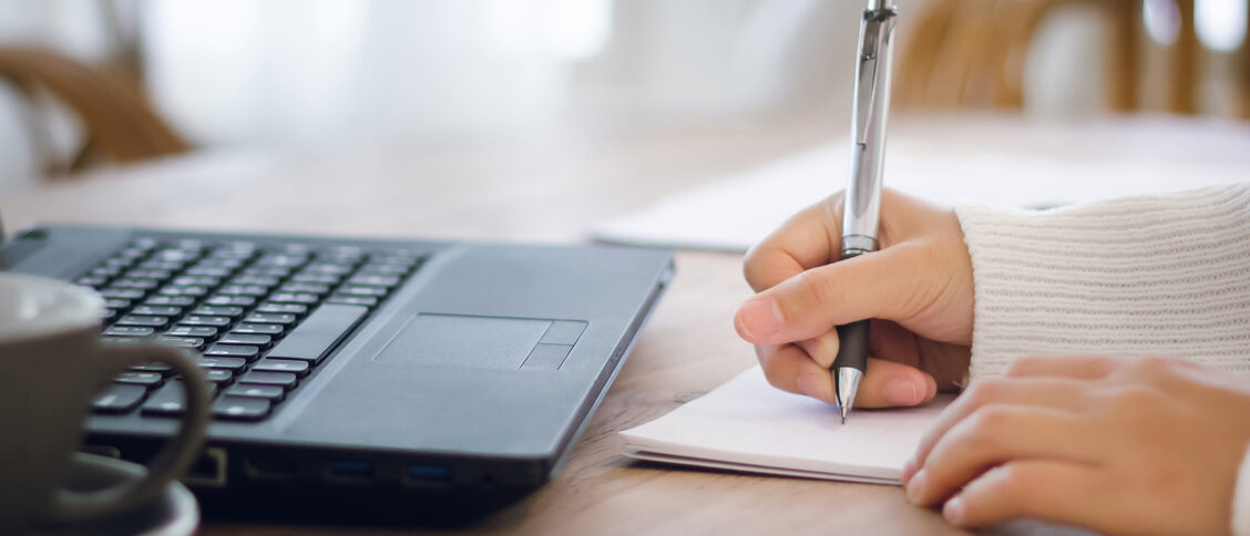 Close-up. girl hand writing on paperwork while she working with laptop on desk