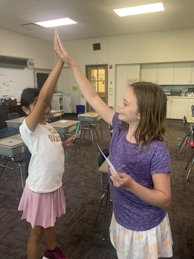 two girls giving each other a high five in a classroom