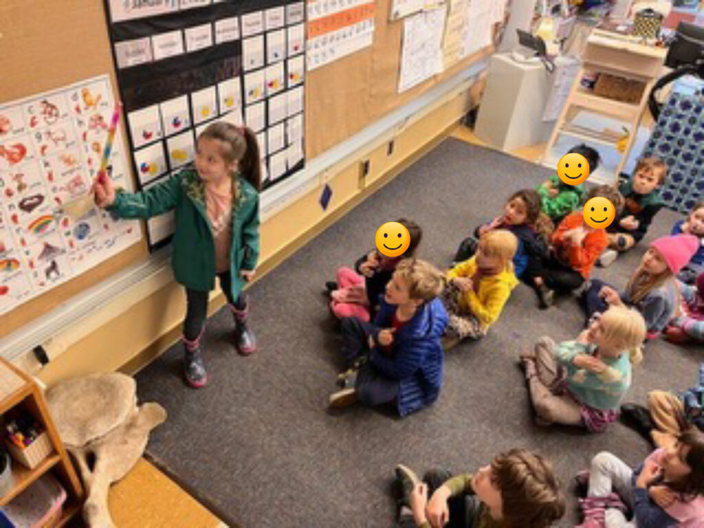 an elementary student stands at a bulletin board making a presentation to her class