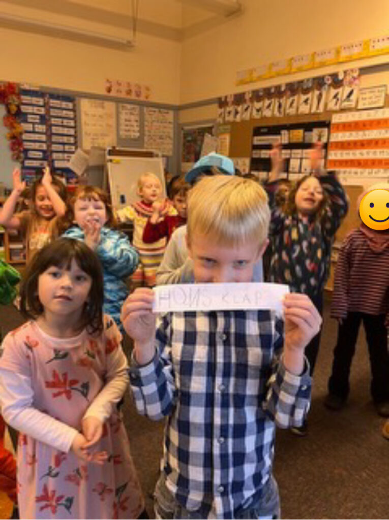 An elementary student standing in front of his class holding a song request for a class dance party