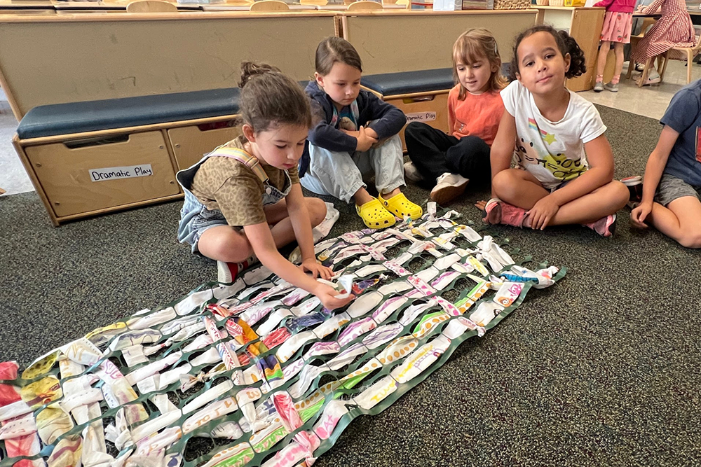 First graders sit on the floor with a completed weaving project