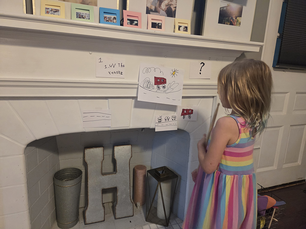 six-year-old girl standing at fireplace looking at art she drew